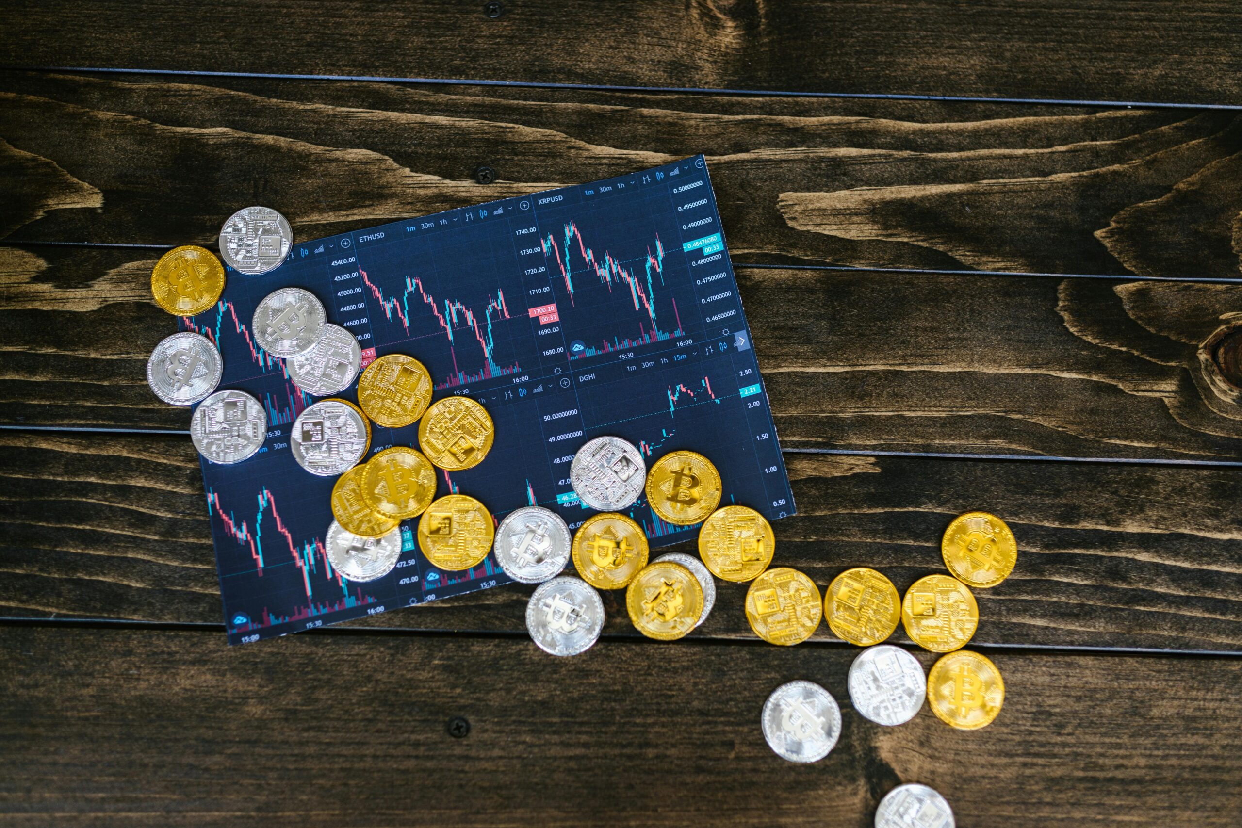 Gold and silver cryptocurrency coins scattered on a trading chart over a wooden table.